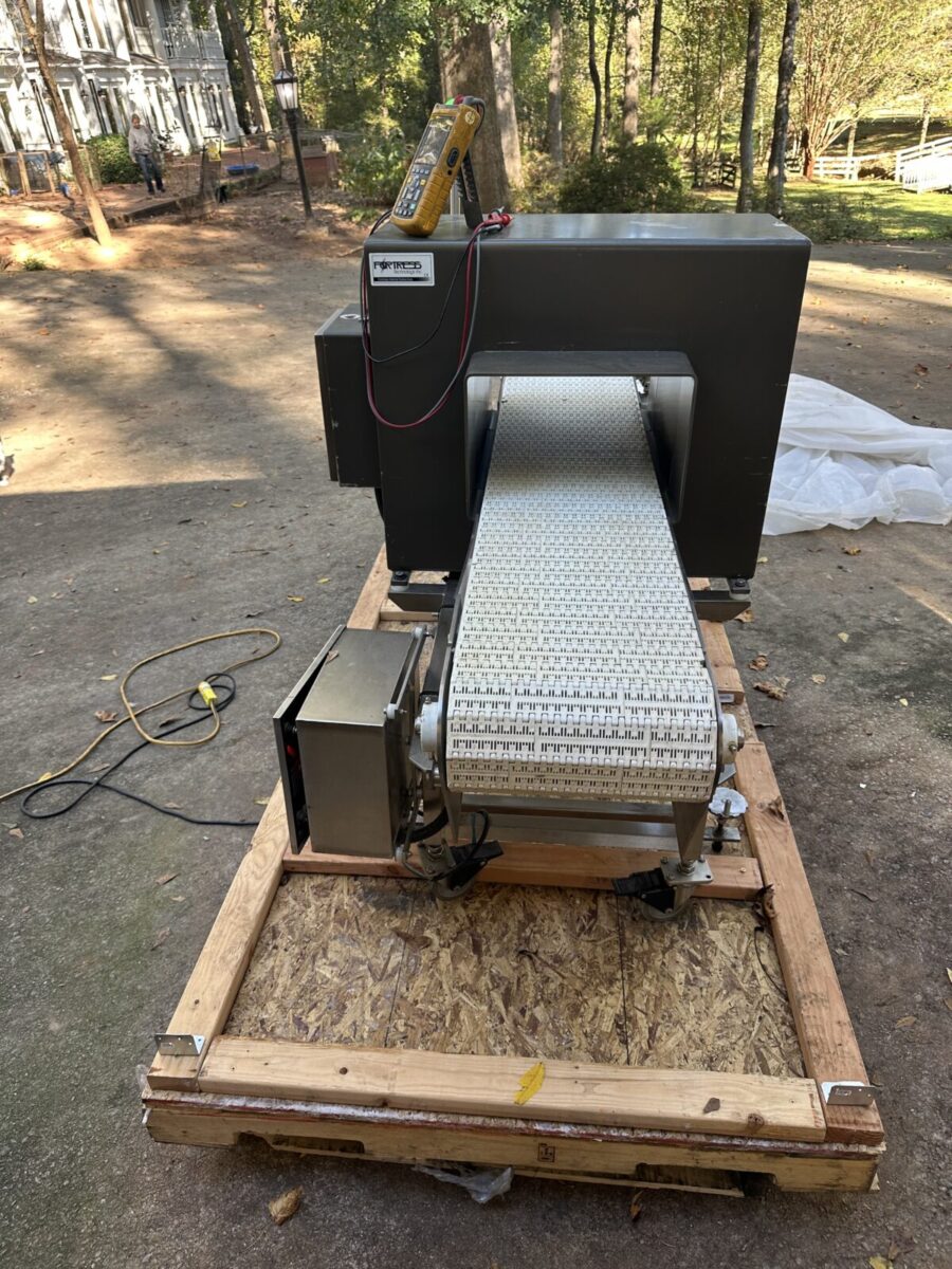 Fortress Belt Stop Conveyor L13899 on a wooden pallet outdoors, with a multimeter resting on top.