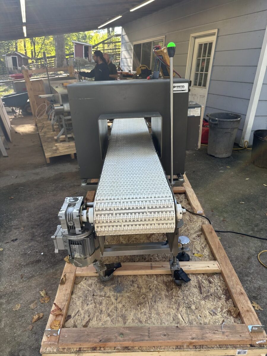 Fortress Belt Stop Conveyor L13899 on a wooden pallet outside, with a worker near equipment and a building in the background.