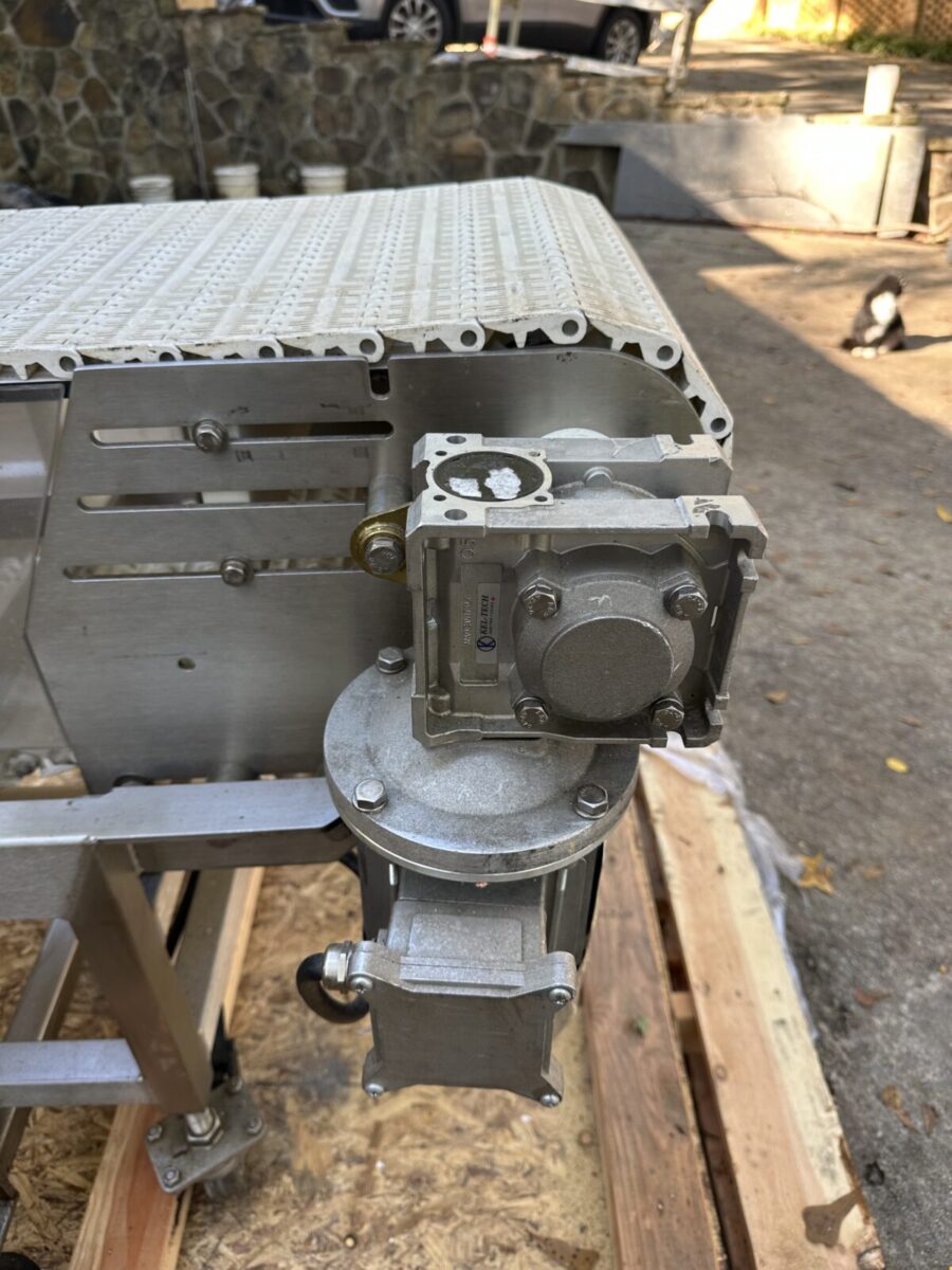 Close-up of Fortress Belt Stop Conveyor L13899 with a metal gear motor on a frame and white perforated platform outdoors.